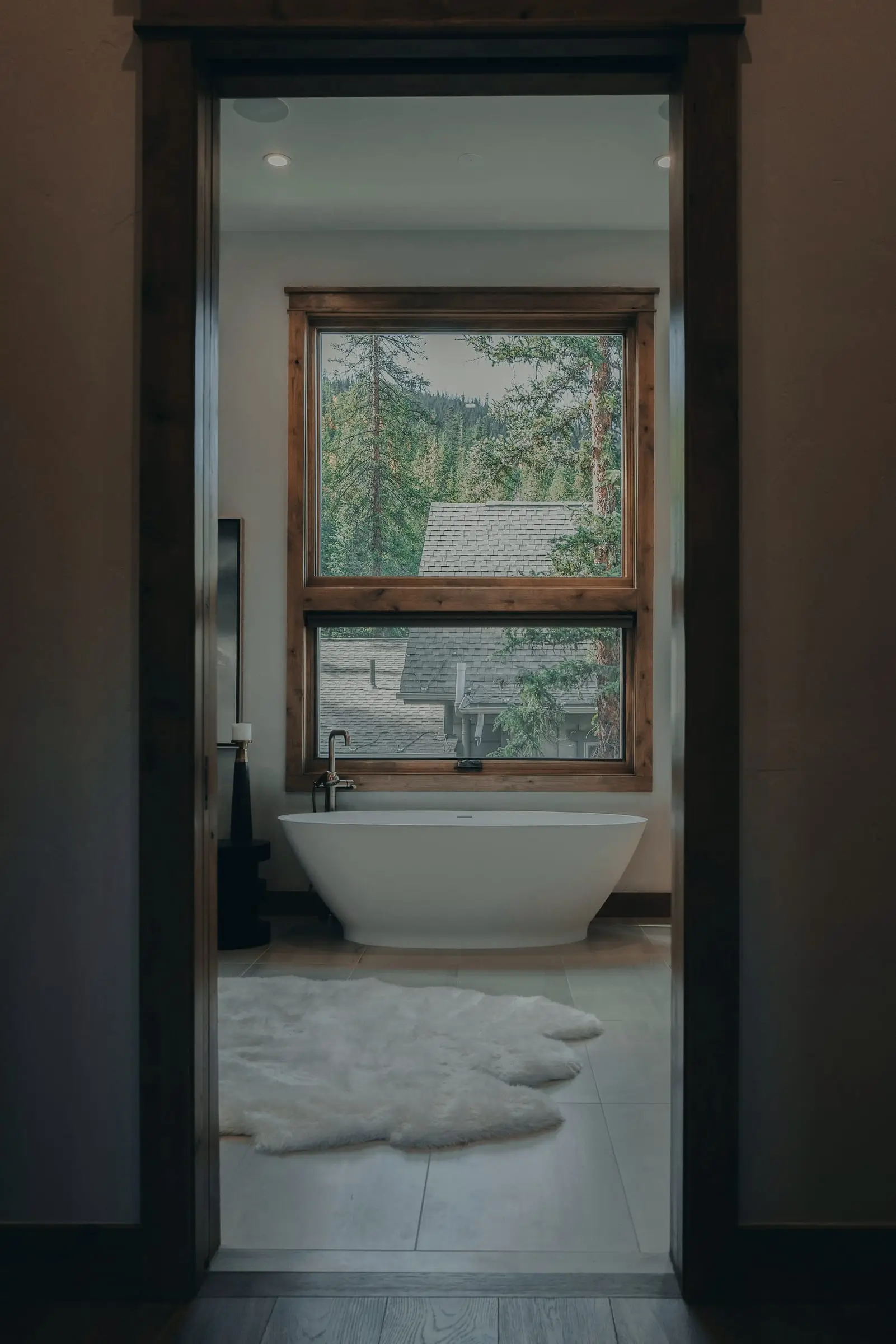 Bañera exenta frente a una ventana con vista a un bosque, vista a través de una puerta.
