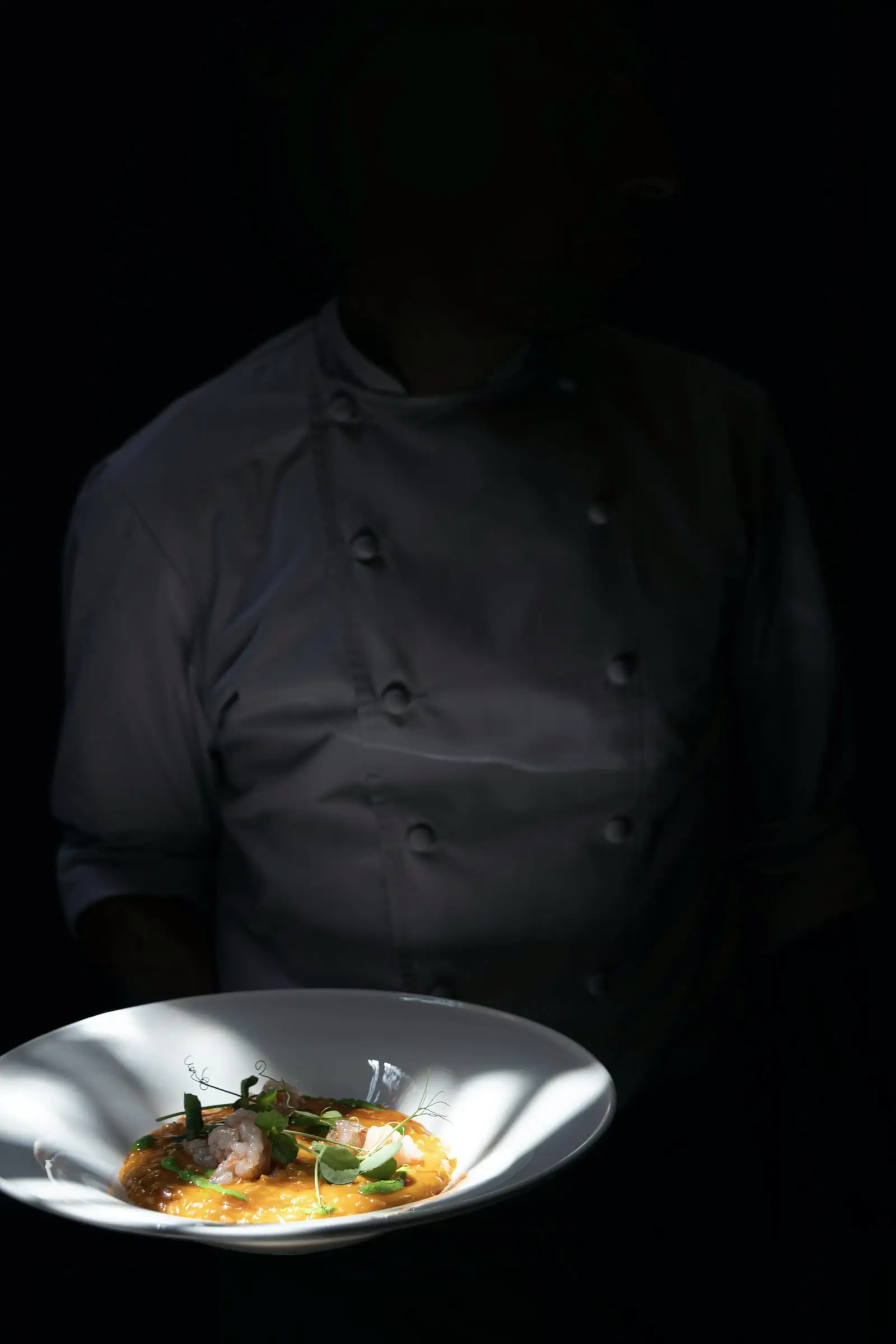 Cocinero en penumbra que sostiene un plato hondo blanco.