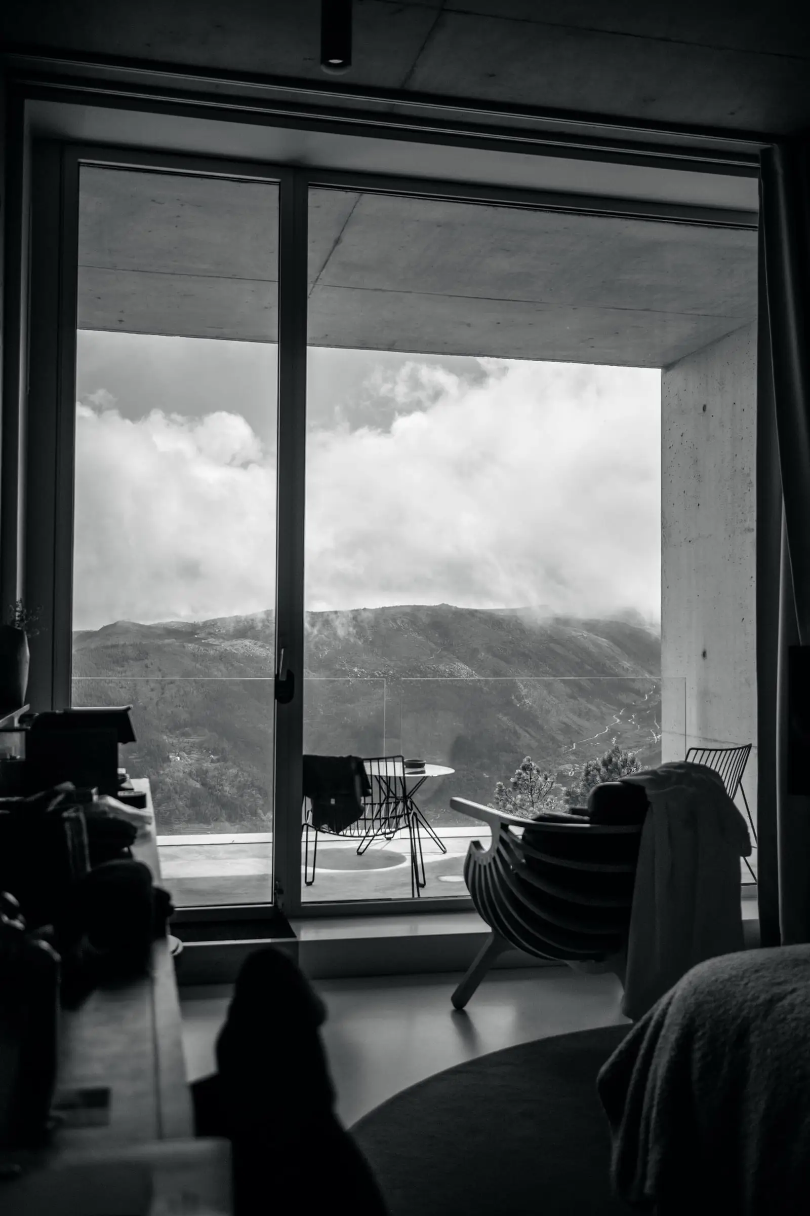 Dormitorio con gran ventanal abierto a un valle de montañas, en blanco y negro.