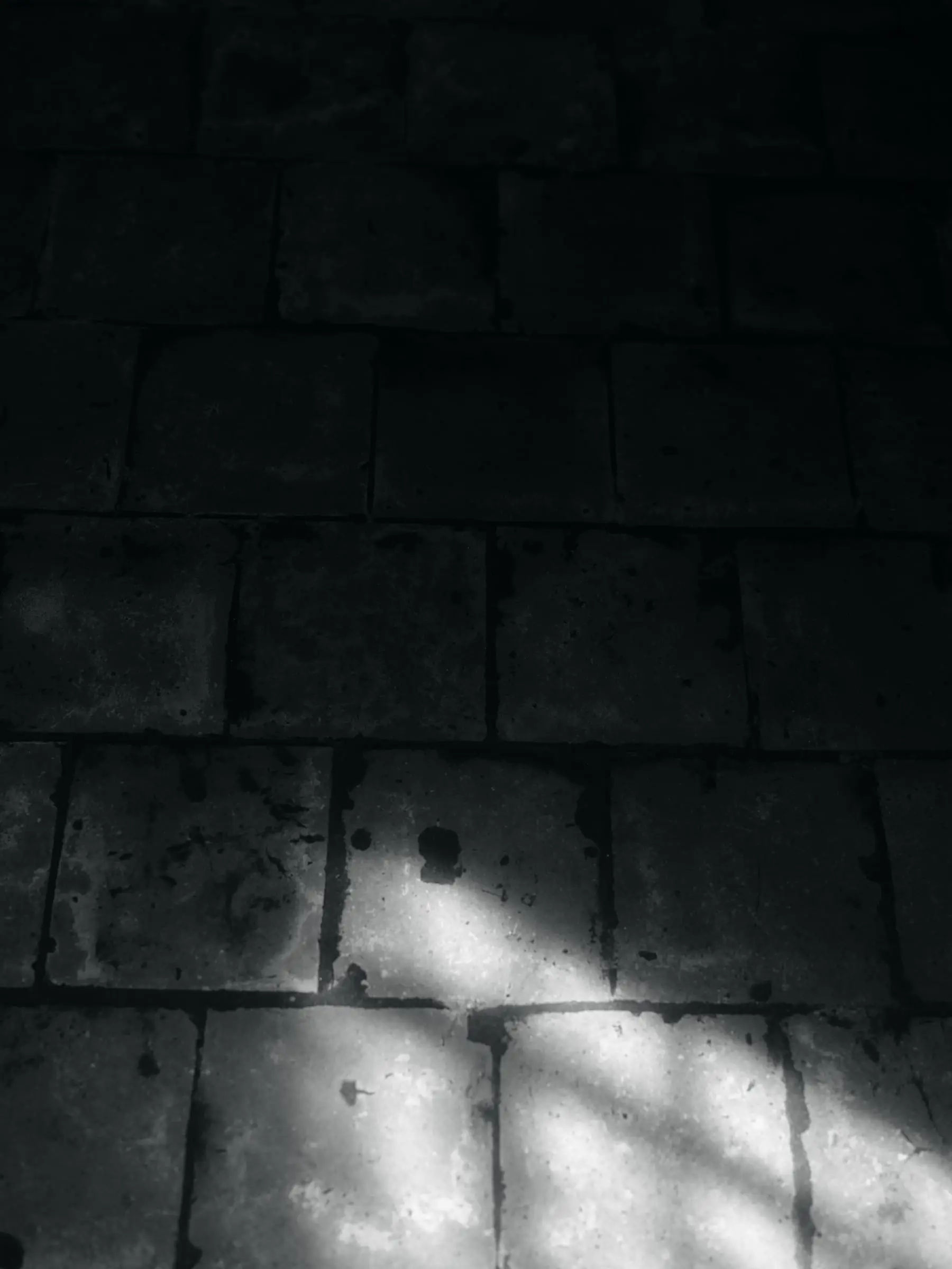 Luz que entra en diagonal sobre un suelo de losas de piedra oscura.