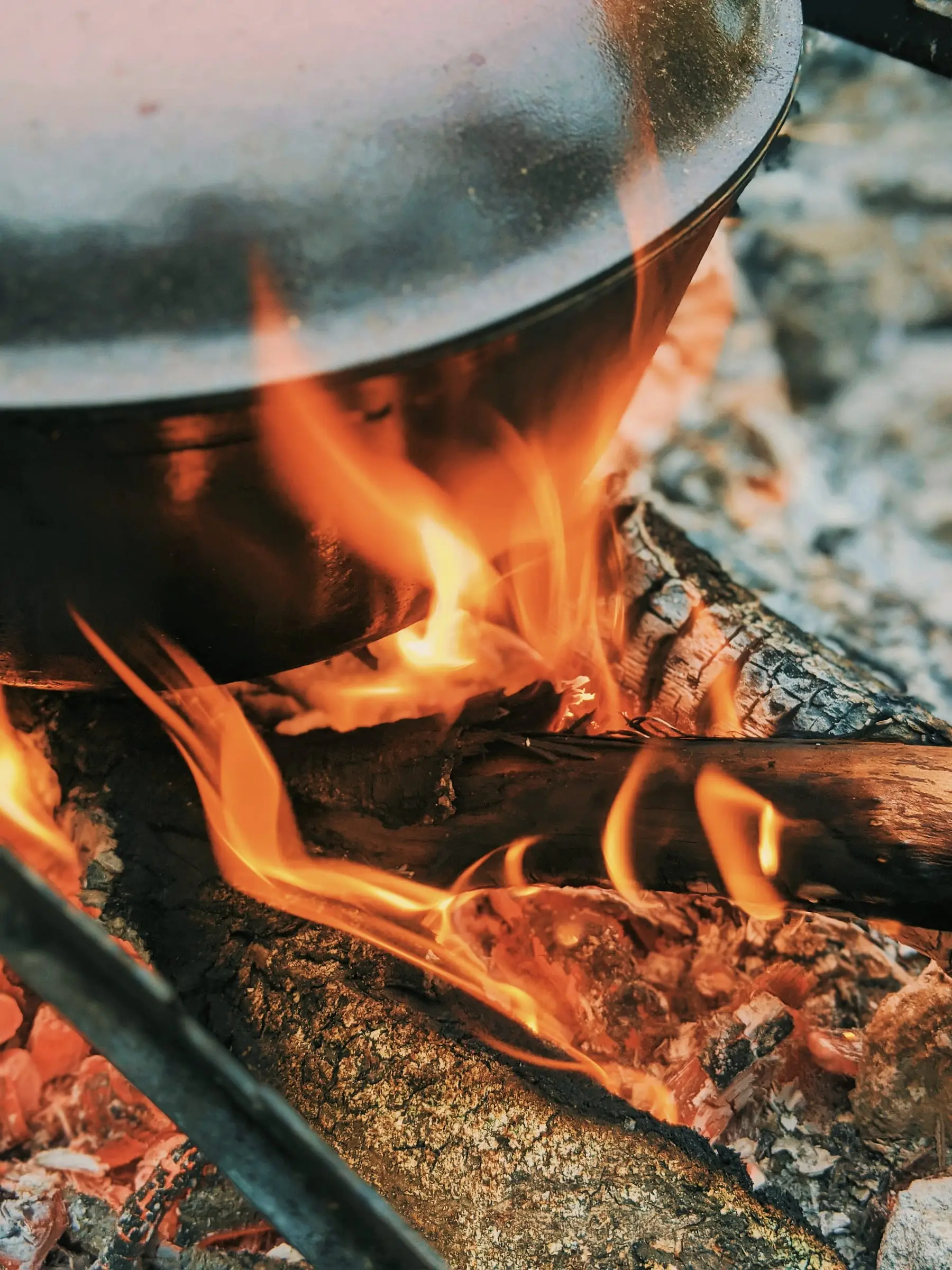 Olla de hierro sobre brasas y leña encendida.