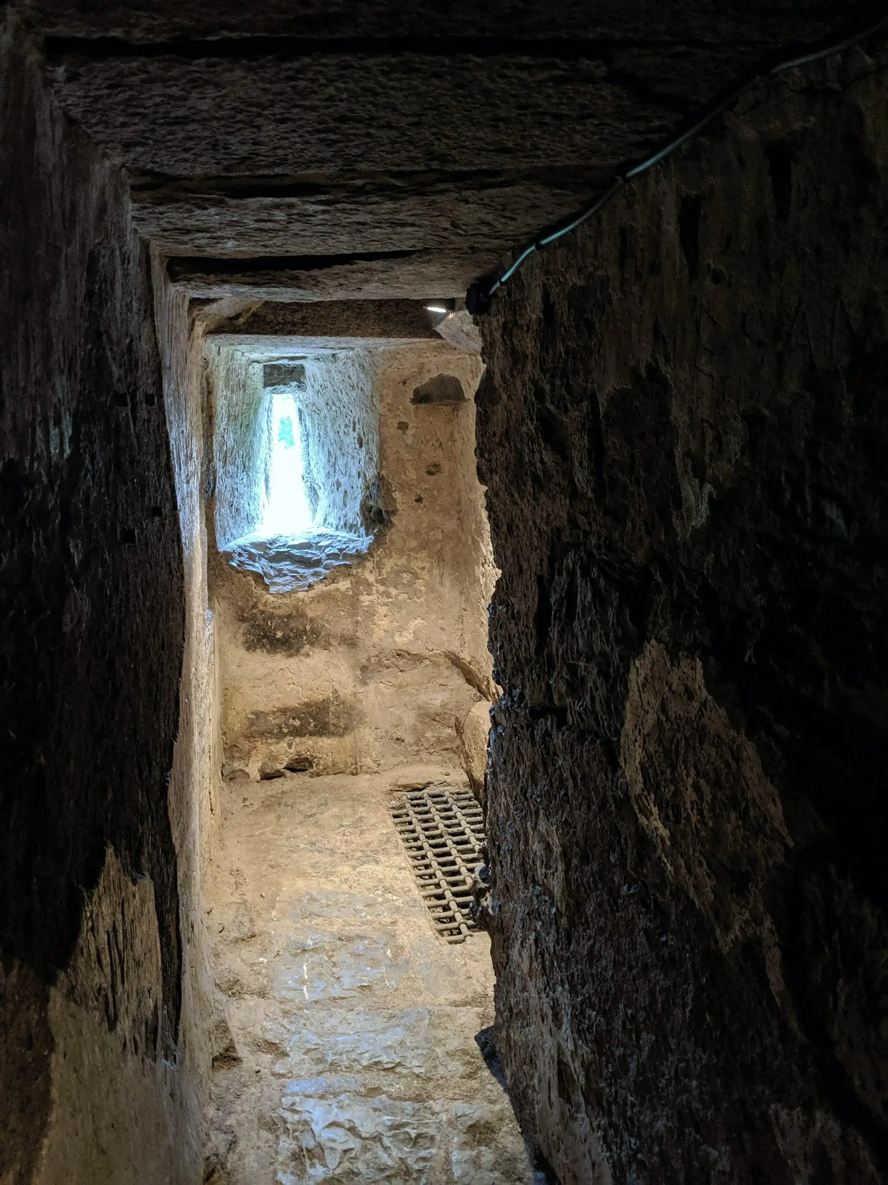 Pasaje estrecho excavado en la roca que termina en una abertura con luz.
