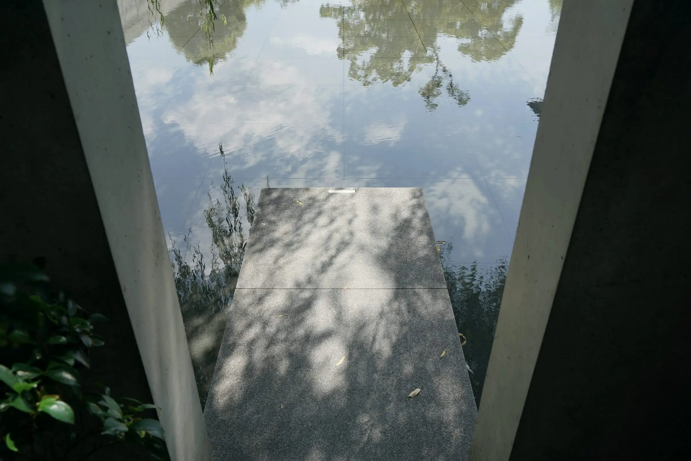 Una pasarela de piedra entra en un estanque que refleja el cielo, entre dos muros.