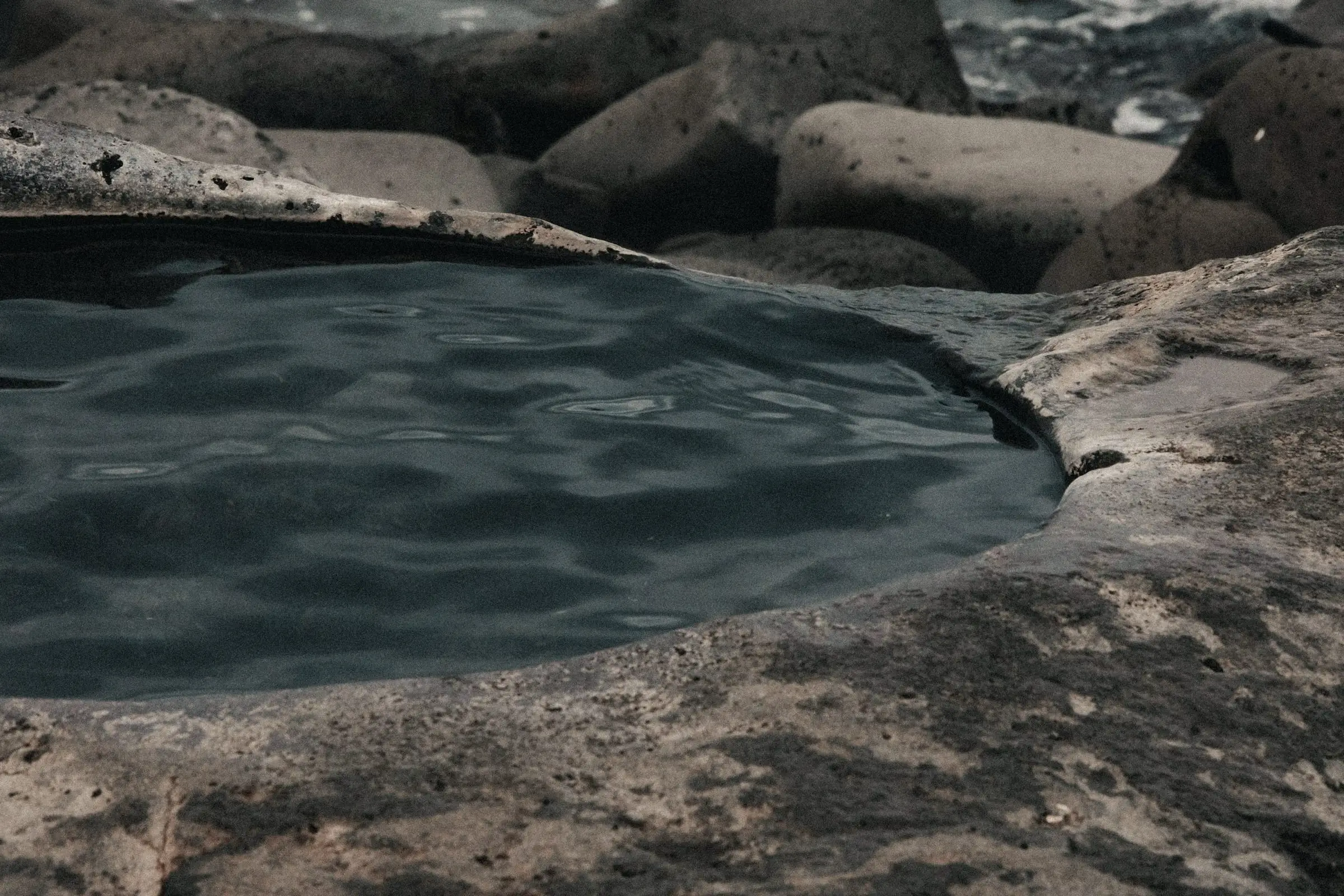Pileta de agua oscura, con la superficie apenas movida, tallada en una roca clara.