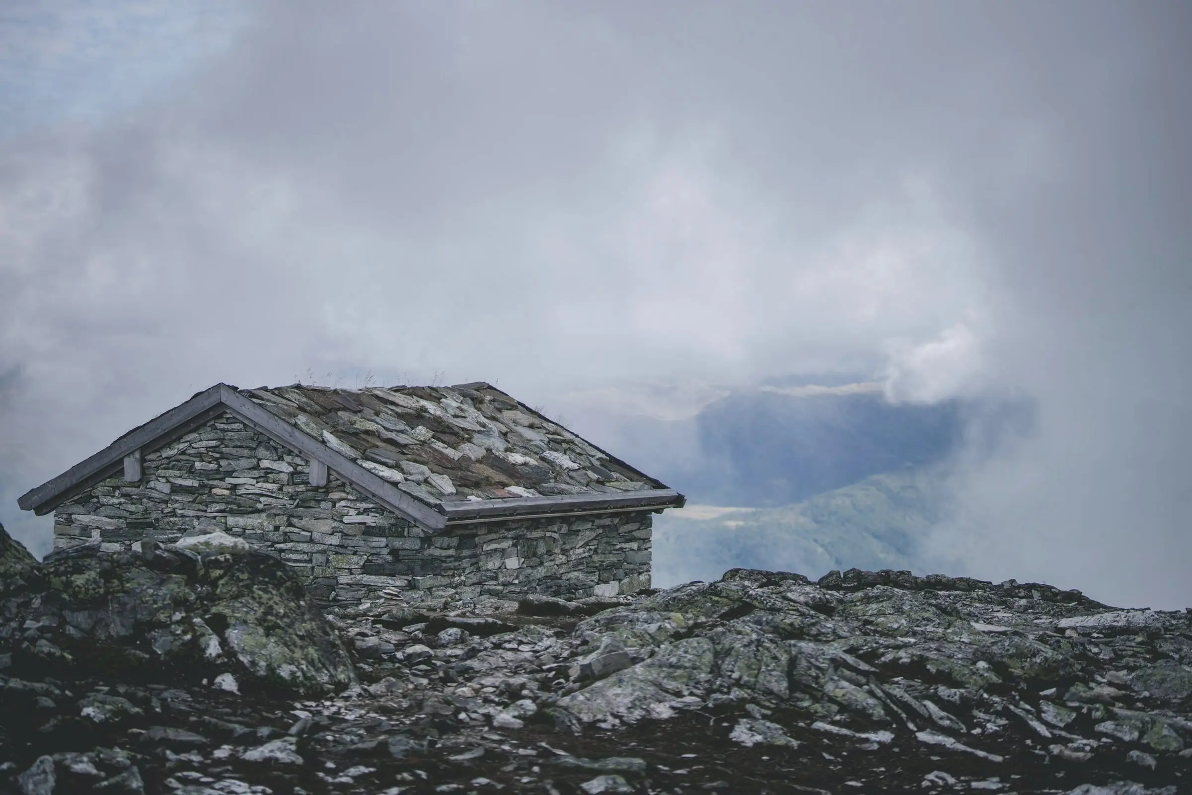 Un refugio de piedra con techo de lajas sobre una loma rocosa, bajo nubes bajas.