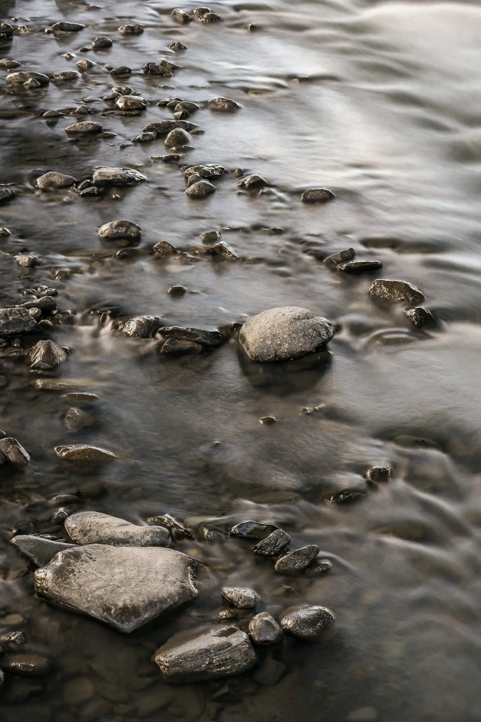 Agua de río que corre sobre piedras redondas, en larga exposición.