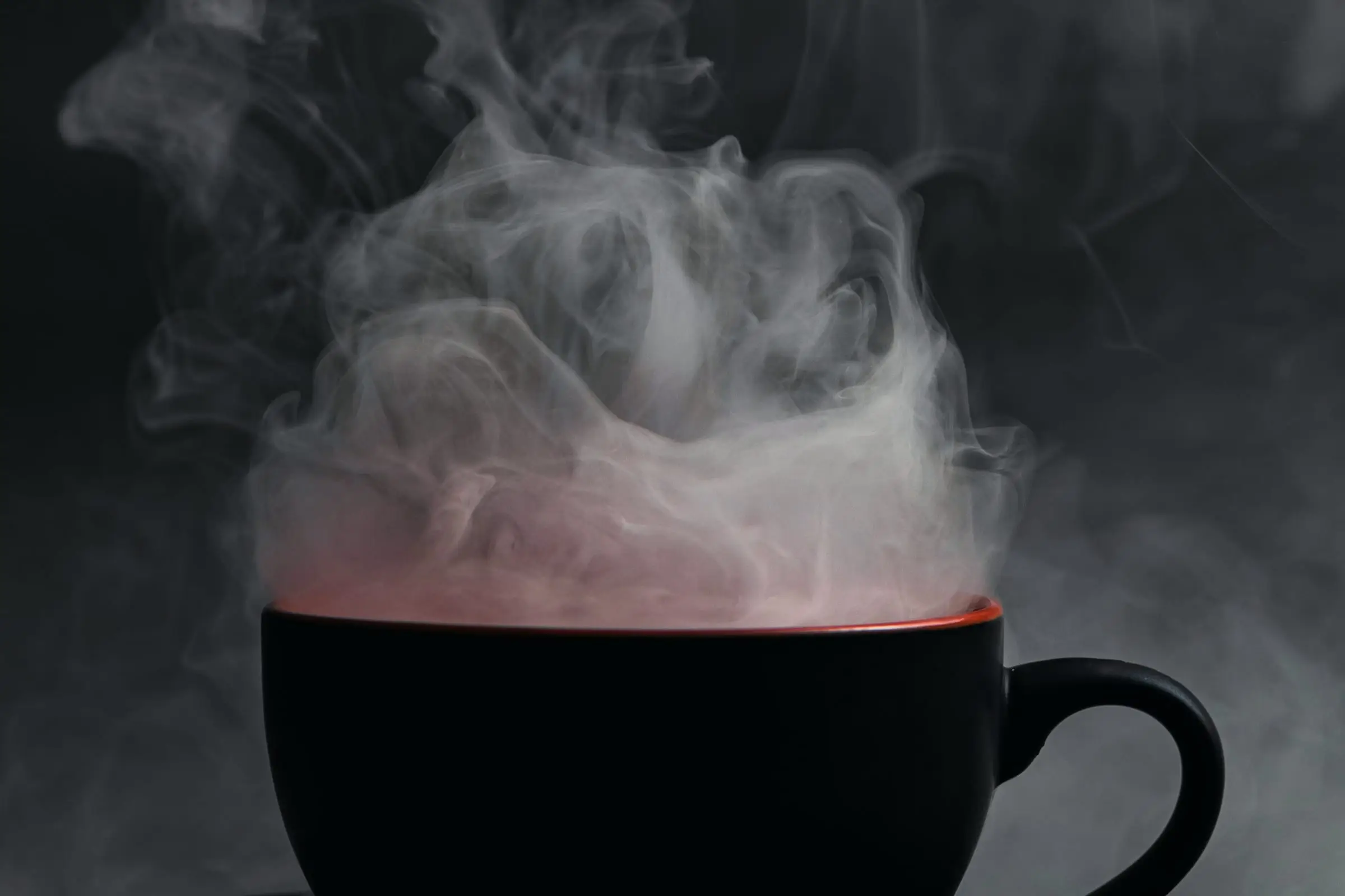 Taza negra con una infusión rojiza de la que sale un vapor denso.