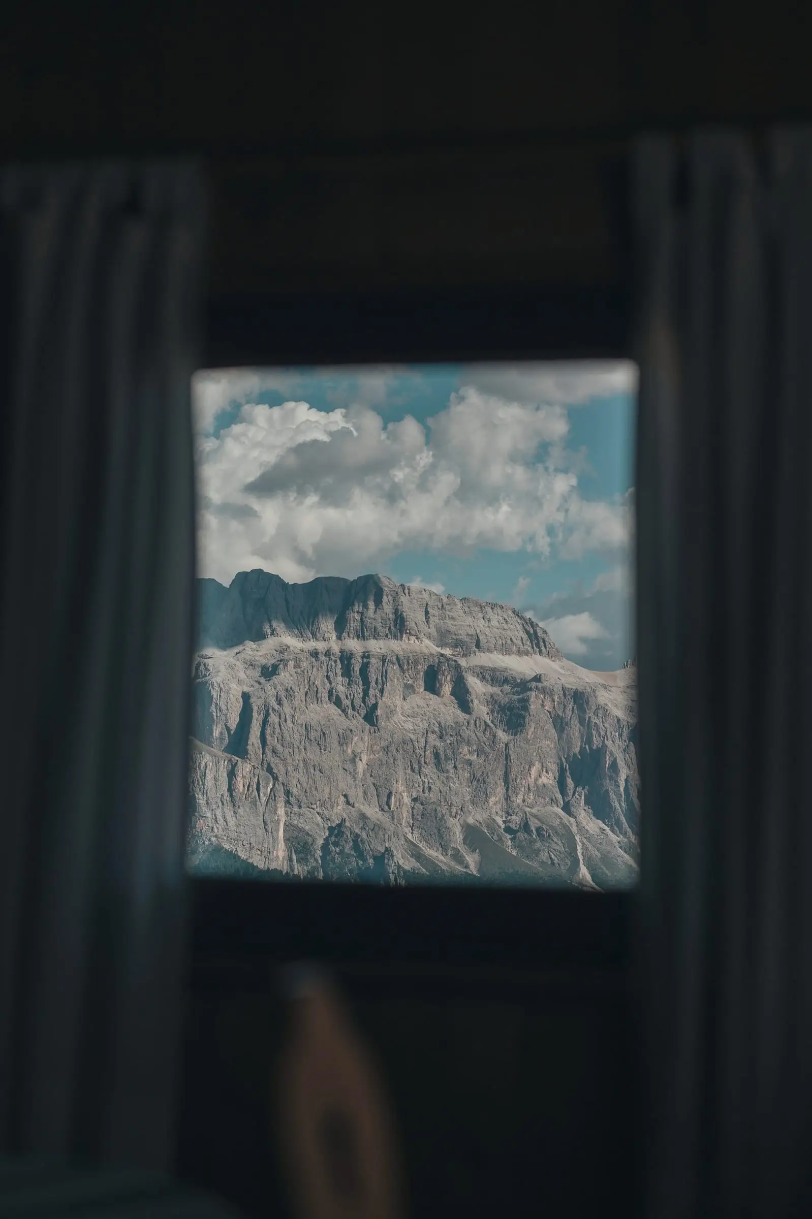 Una cortina oscura abierta deja ver una pared de roca bajo un cielo con nubes.