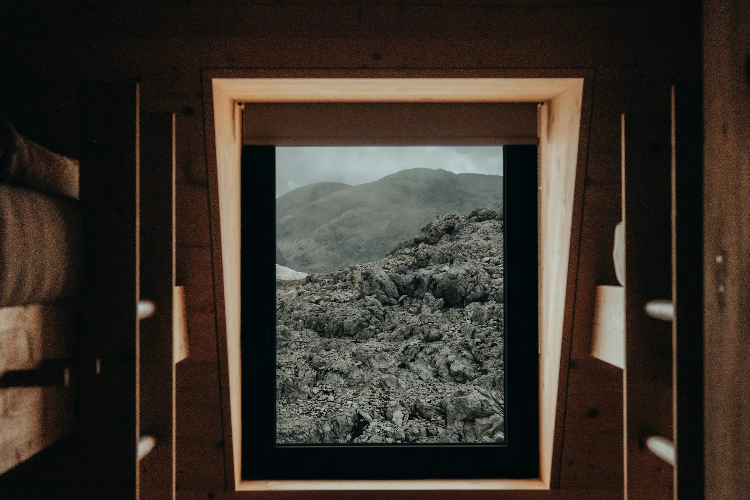 Ventana con marco de madera oscura que encuadra un campo de lava y lomas verdes.