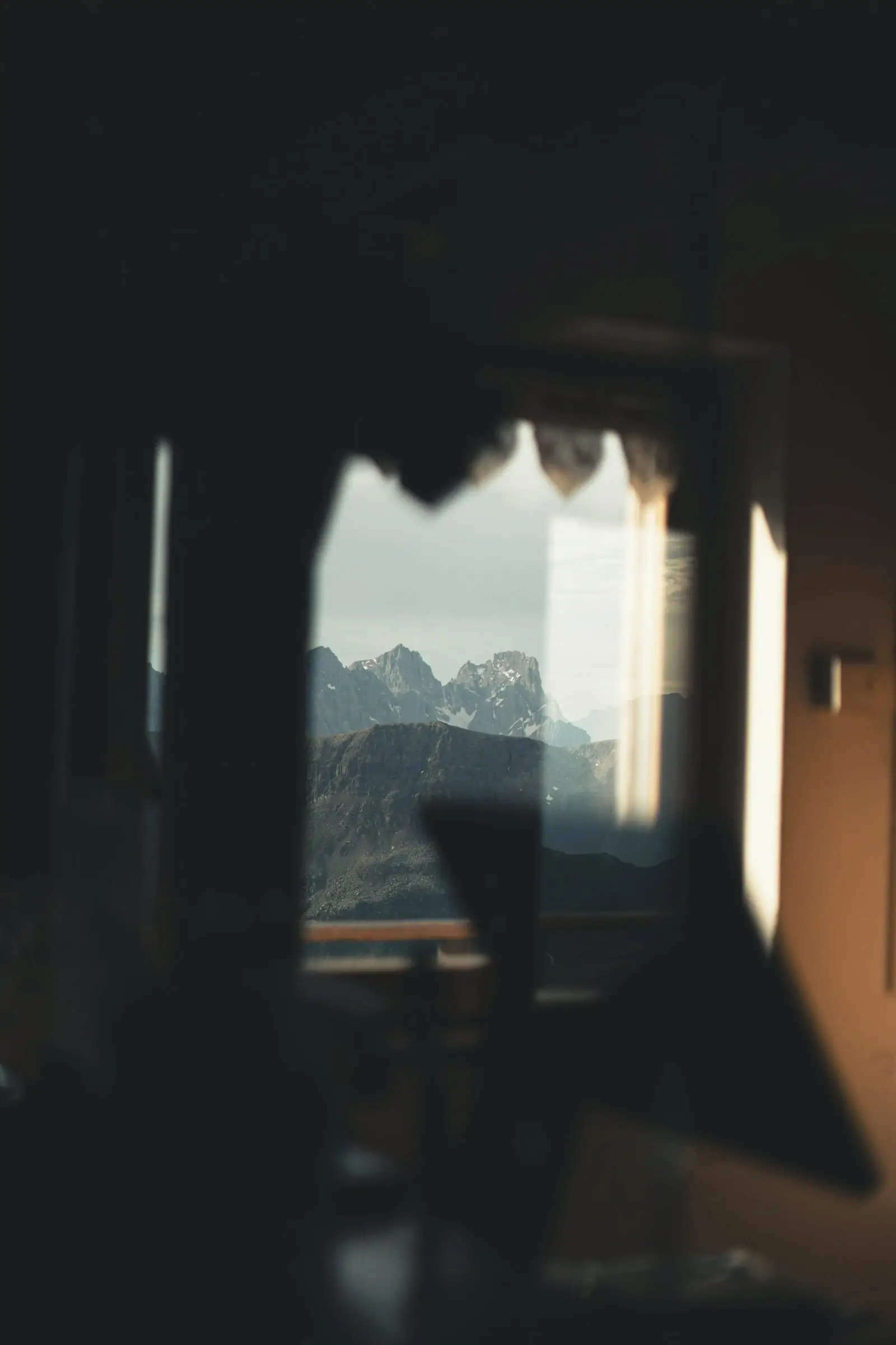 Habitación en penumbra con una ventana por la que se ven picos lejanos.