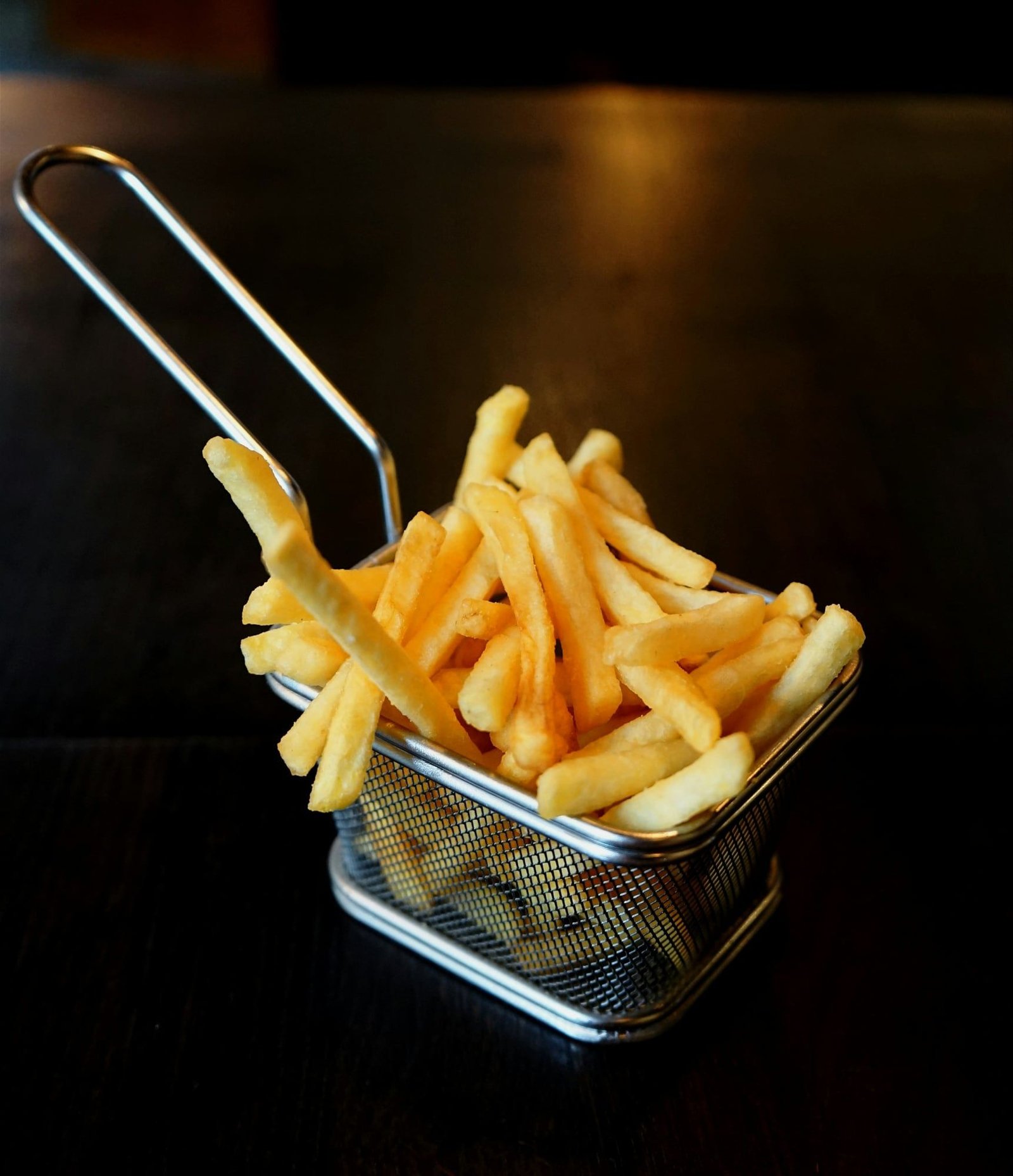 Papas fritas doradas en una canasta de metal, sobre fondo negro.