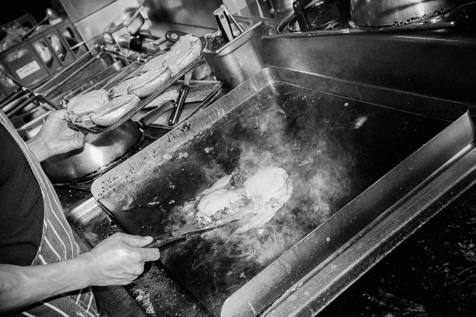 Plancha de cocina con medallones y humo, en blanco y negro.