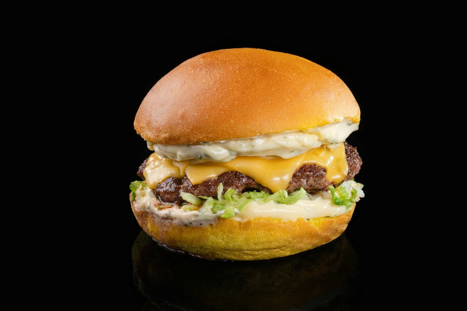 Hamburguesa simple en pan brioche con cheddar, mayonesa de hierbas y lechuga, sobre fondo negro.