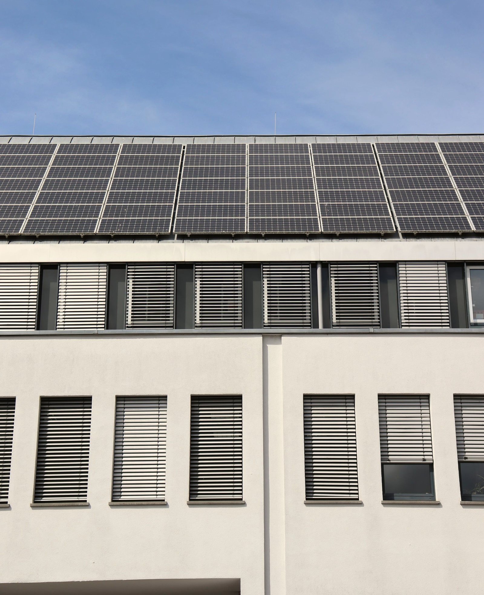 Edificio blanco de oficinas con persianas y una cubierta inclinada cubierta de módulos solares.