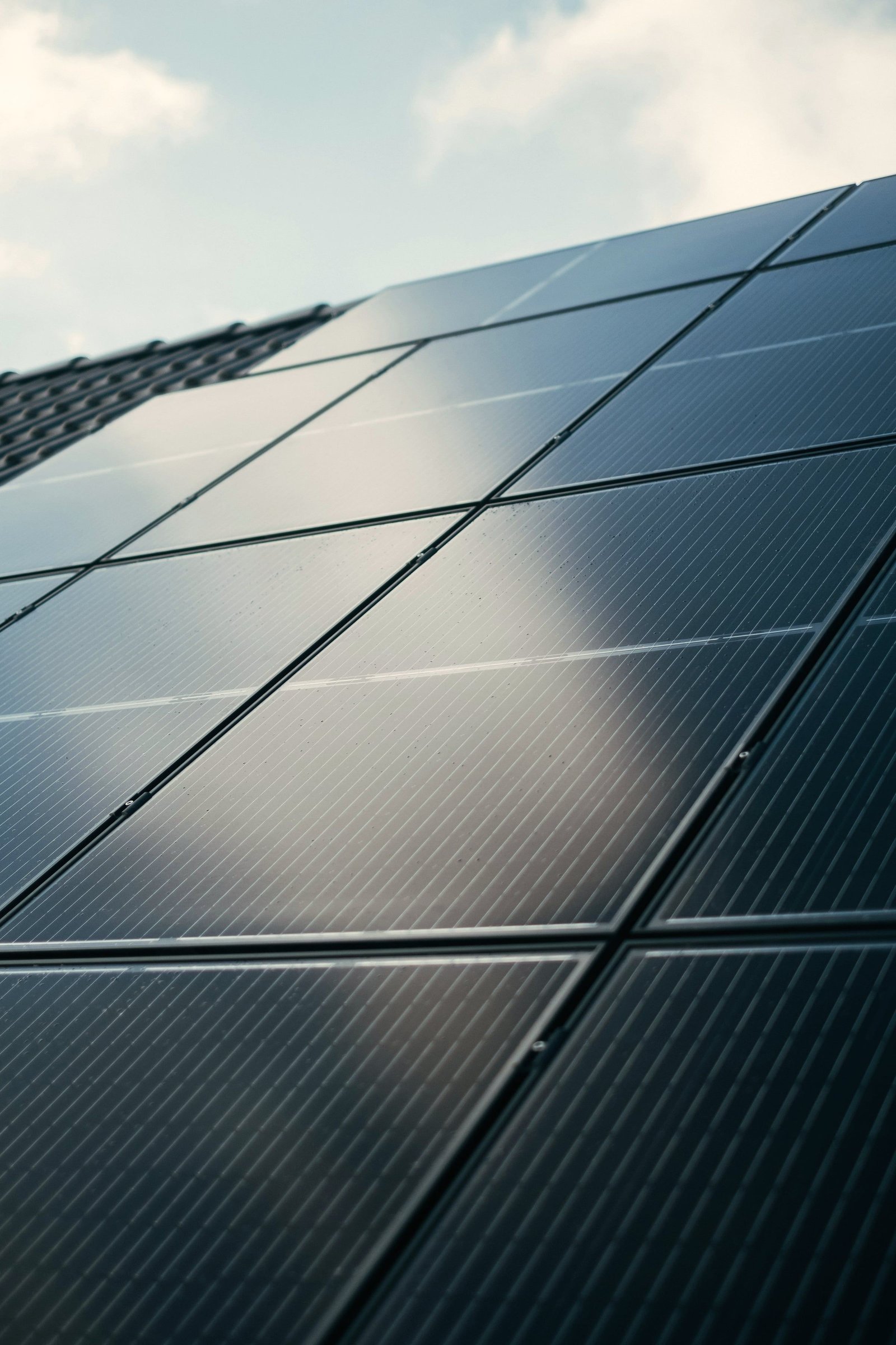Detalle de módulos solares oscuros en una cubierta inclinada que reflejan el cielo y las nubes.