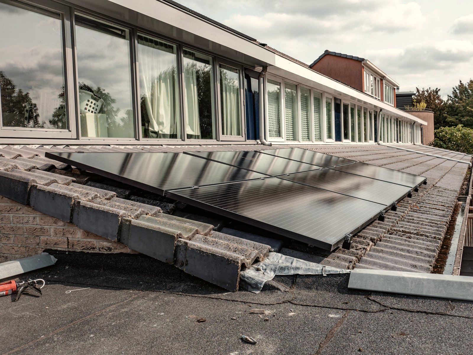 Módulos solares recién colocados sobre soportes en una cubierta plana, junto a las ventanas de un edificio.